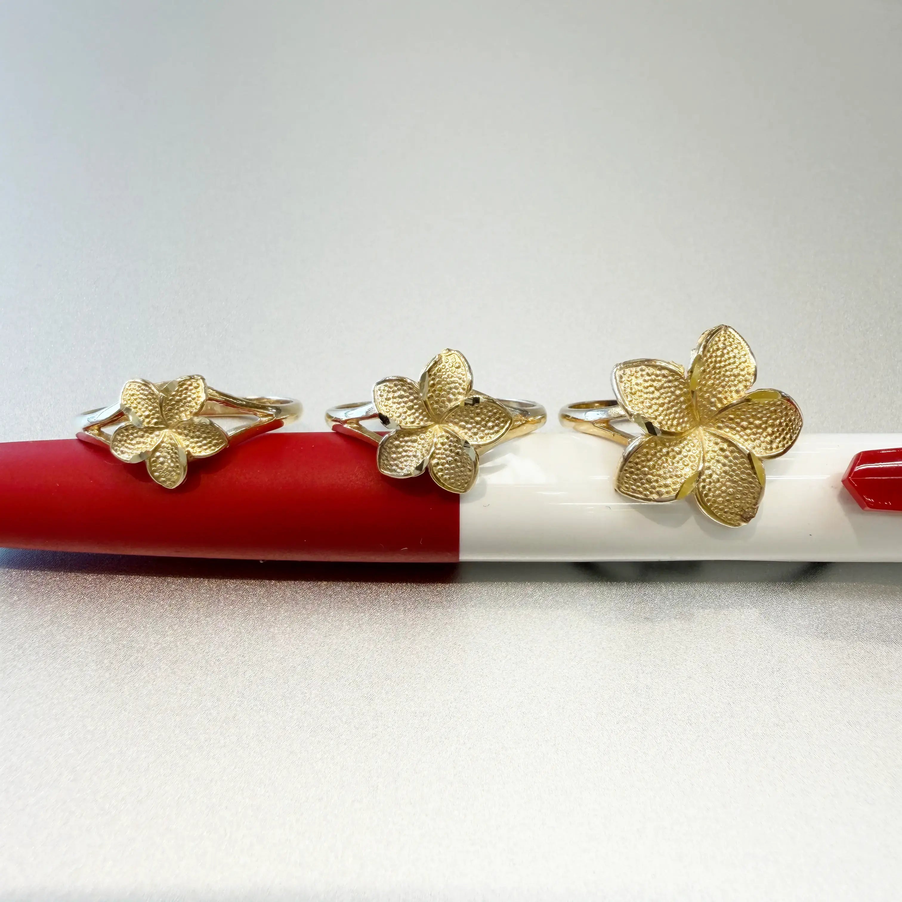 14K yellow gold plumeria flower rings in small medium and large sizes side by side on white background